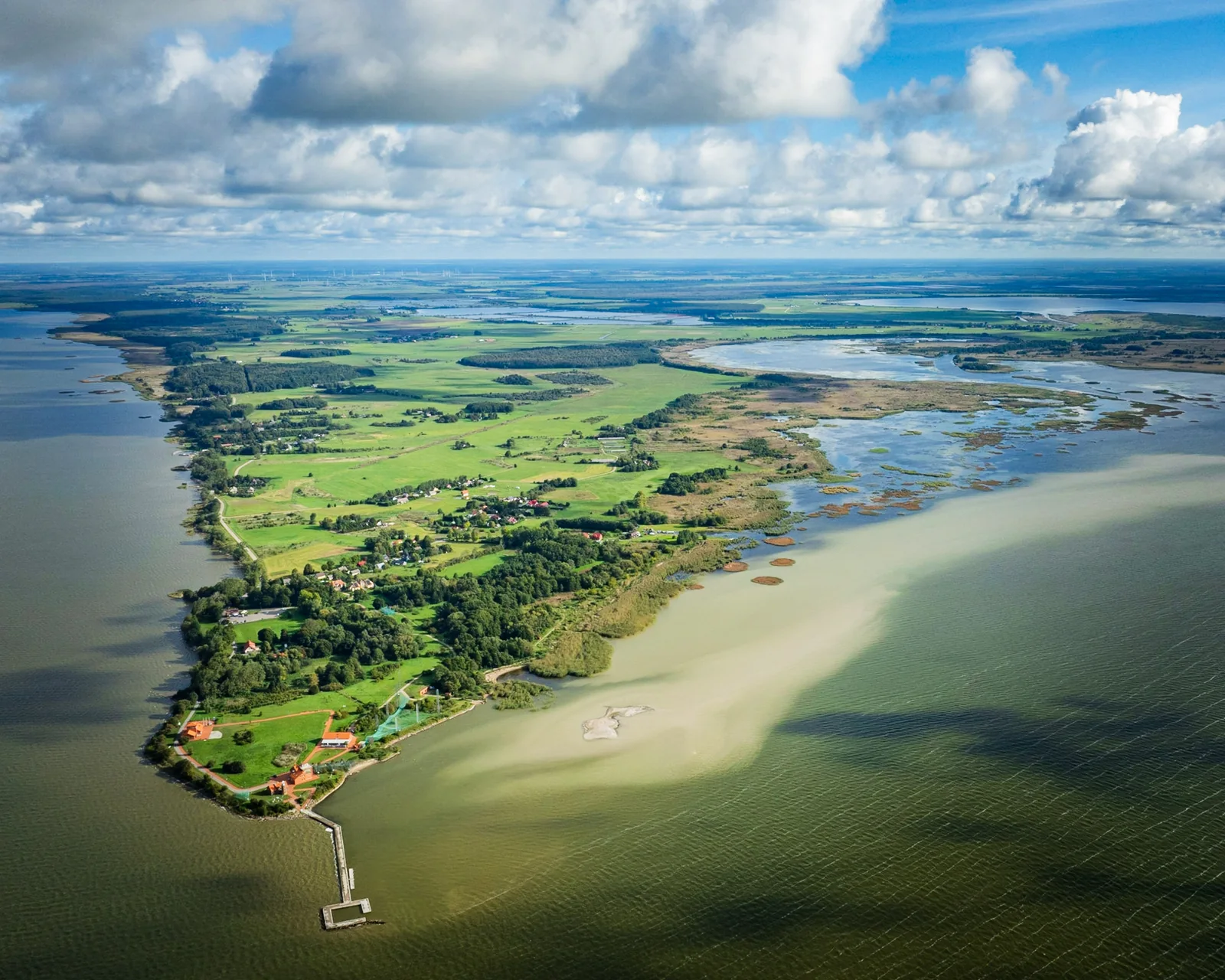 Aerial view of Ventės ragas peninsula, with a pier, green fields and reed beds beside the Curonian Lagoon.