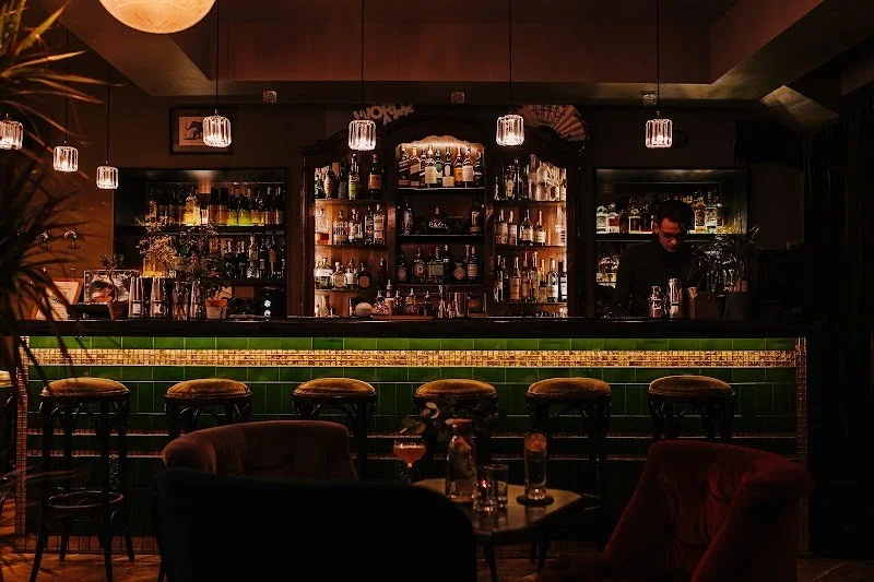 Green-tiled bar counter and illuminated shelves at Nomads Cocktail Bar.